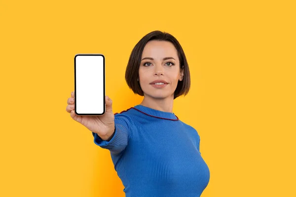 モバイル広告 白い画面で空白のスマートフォンを示す美しい若い女性 空の携帯電話を実証 新しいアプリやウェブサイトをお勧めします 黄色の背景に孤立立ちます モックアップ — ストック写真