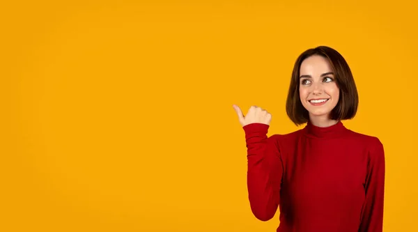 伟大的提议或交易 年轻而快乐的女士 有着可爱的红头发 手指指向空旷的广告或文字空间 面带微笑 橙色的工作室背景 — 图库照片
