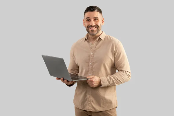 stock image Happy middle aged businessman in shirt chatting with client by laptop looking and smiling at camera posing on grey studio background, free space. Business and gadgets lifestyle concept