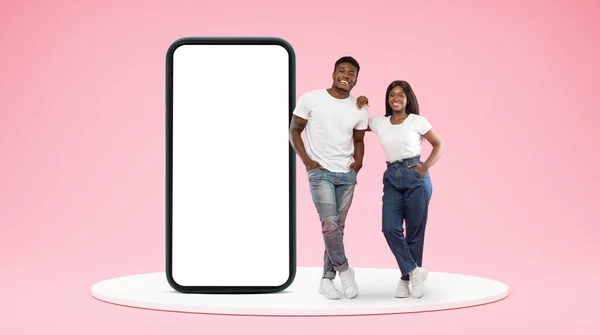 自信地微笑着 千年非洲裔美国夫妇 拥有巨大的智能手机 舞台上的空白屏幕 背景是粉红色的 App Recommendation Blog Website — 图库照片