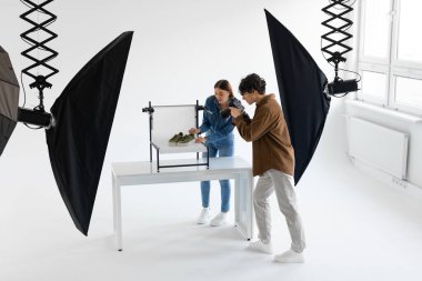 Professional team of photographer and content manager shooting stylish shoes in photostudio, working together, full length shot, free space clipart