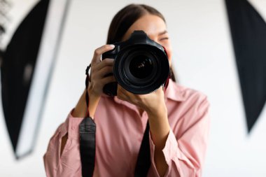 DSR kameralı genç bir kadın stüdyoda ışıklandırma ekipmanıyla fotoğraf çekiyor, kadın fotoğrafçı profesyonel kamerayla fotoğraf çekiyor, yakın plan.