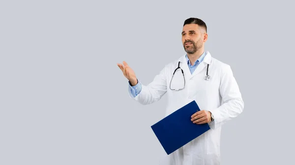 医疗服务概念 穿着制服的男医生 手里拿着剪贴板 一边看一边说话 摆出灰色背景 带着复印空间 — 图库照片