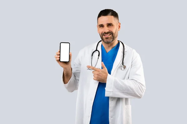 Cheerful Middle Aged General Practitioner Man Uniform Pointing Cellphone Blank — Stock Photo, Image