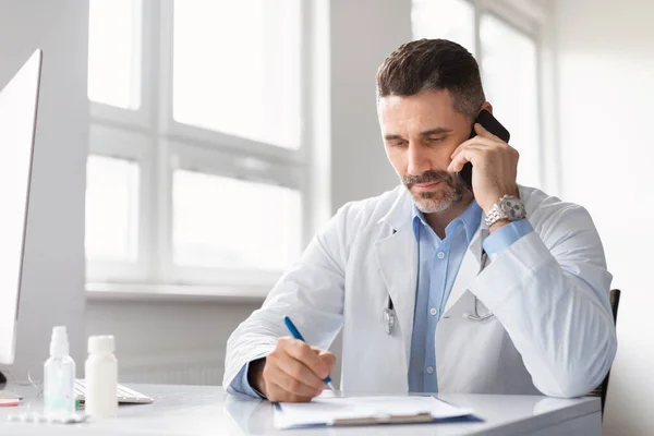 Focused Male Doctor Talking Cellphone Patient Writing Clipboard Taking Notes — Stock Photo, Image