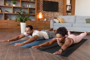 Spor giyim sektöründe genç ve mutlu bir zenci kadın ve koca yerde yatıp birlikte oturma odasının içinde antrenman yaparken eğleniyorlar. Spor salonu, yeni normal, vücut bakımı, zayıflama yaşam tarzı ve evdeki fitness