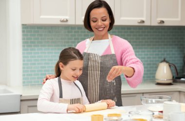 Neşeli beyaz anne ve önlüklü küçük kız mutfak içinde merdane ve unla kurabiye hamuru yapıyorlar, fotokopi alanı. Yemek pişirme dersi, ev yapımı tatlılar.