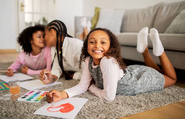 快乐的黑人小女孩与妈妈和姐姐在一起画画 在家里客厅的地板上粘合 开心的躺在地板上 微笑着拍照 家庭周末休闲概念 浅层深度 — 图库照片