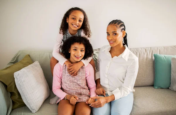 Black Mommy Daughters Hugging Sitting Sofa Smiling Camera Home Positive — Stock Photo, Image