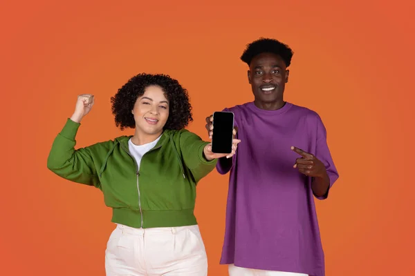 キャッシュバック宝くじ 感情的に幸せな若い多文化カップル黒男とヒスパニック系の女性ショー携帯電話で空の黒画面 ジェスチャーや笑顔 ギャンブルオンライン 赤の背景 — ストック写真
