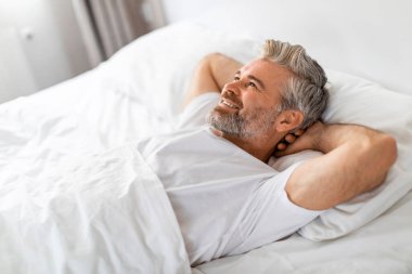 İyi dinlenmiş, yakışıklı, sakallı, gri saçlı, orta yaşlı, pijama giyen, sabah uyandıktan sonra dinlenen, fotokopi odasına bakan ve gülümseyen, yeni güne hazır, yan görüş