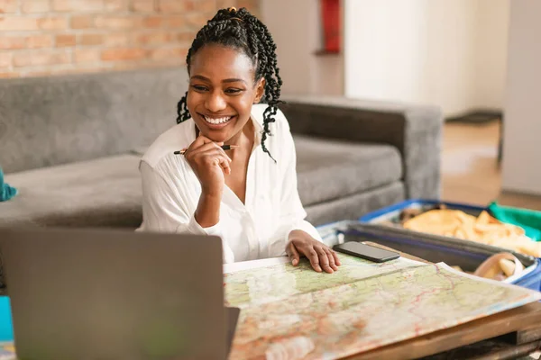 ラップトップと地図で幸せな黒の女性の計画休暇 満員のスーツケースの近くに座って 将来の旅のための最高の旅行ルートをチェックし 旅行の準備 スペースのコピー — ストック写真