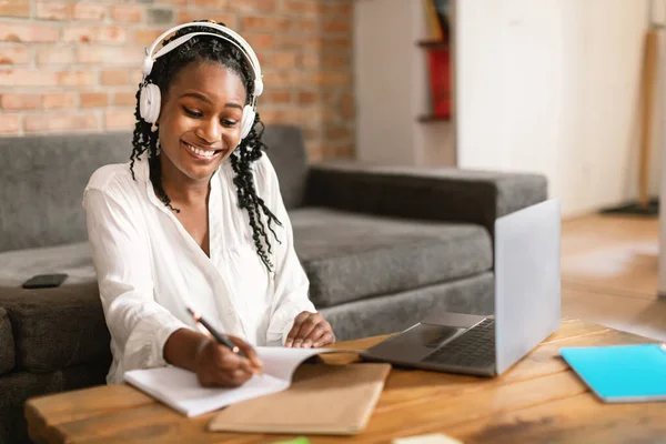 ノートを取り ノートパソコンの前に座って ヘッドフォンを着て コピースペースを着て 自宅からオンラインで勉強する幸せなアフリカ系アメリカ人女性 現代の距離教育と技術 — ストック写真
