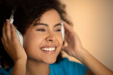 Bin yıllık mutlu Afro-Amerikan kıvırcık saçlı kablosuz kulaklıklı kadının yüzü müzik dinler, oda içi boş zamanların tadını çıkarır, kapar, kırpar. Eğlence, dinlenme ve rahatlama, ders ve ders, ses uygulaması