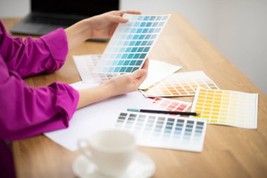 Tasarımcı kadının ev ofisinde renk örnekleriyle çalışması, tanınmayan bir kadının masasında oturup renk paletini kontrol etmesi, yeni tasarım projesi için dekorasyon seçmesi, yakın plan...
