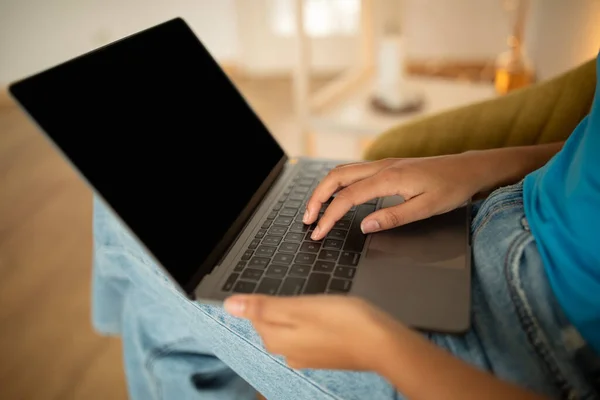 Millennial african american lady typing on laptop with blank screen in living room interior, cropped, close up. Work, study, business, freelance remotely and online shopping at home