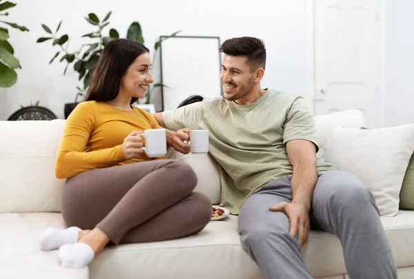 一緒に愛のお茶を飲む若いカップルは リビングルームでソファに座って 家庭でコーヒーを楽しむ家庭用の幸せな美しいヒスパニック系の男性と女性は コピースペースを持っている — ストック写真