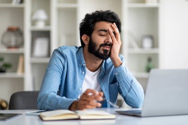 Çok çalışan Hintli erkek girişimci, ofis masasında otururken yorgun hissediyor. Uykulu, genç, doğulu bir adam iş yerinde kestiriyor. Dizüstü bilgisayarla çalıştıktan sonra bitkin düşüyor.