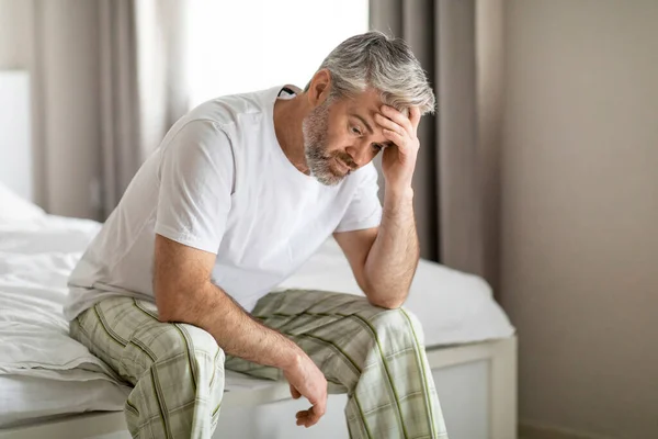 忧心忡忡的中年白发苍苍的英俊男人穿着睡衣独自坐在床上 摸着头 患有宿醉或焦虑 复制空间 中年危机 — 图库照片