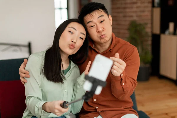 韓国の感情的なカップルは 面白い自撮りや携帯電話のウェブカメラでは リビングルームのソファの上に座って優雅さを取る 中年男性と若いです女性キャプチャ瞬間上の写真 — ストック写真