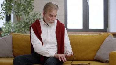 Yaşlı sakallı adam kan oksijeni seviyesini dijital nabız oksimetresiyle ölçüyor, evdeki sağlık durumunu kontrol ediyor, boş bir alanda. Astım, akciğer hastalığı..