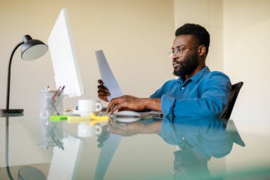 Gazeteleri ve iş raporlarını okuyan, işyerinde bilgisayarın önünde oturan, fotokopi çeken siyahi bir işadamı. Başarılı girişimcilik kariyeri, muhasebe ve belgeler