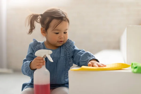 Spring Cleaning. Cute Korean Baby Girl Holding Detergent Bottle Dusting And Mopping Floor With Rag In Clean Room At Home. Adorable Child Doing House Chores. Selective Focus