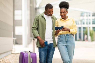 Tatil seyahati. Mutlu Afrikalı Amerikalı Gezginlerin pasaportları var. Uçuş biletlerini ve belgelerini kontrol ediyorlar. Bavulları modern havaalanına yakın bir yerde duruyor.