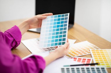 Ofiste renk örnekleriyle çalışan tanınmayan kadın tasarımcı, genç bir kadının masa başında oturup yeni tasarım projesi için renk paleti seçerken kırpılmış görüntüsü, yakın plan.