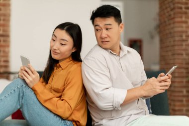 Meraklı orta yaşlı bir adam karısının cep telefonuna bakmaya çalışıyor. Kadın alet kullanıp sohbet ediyor. Bir çift arka arkaya oturma odasındaki koltukta oturuyor.