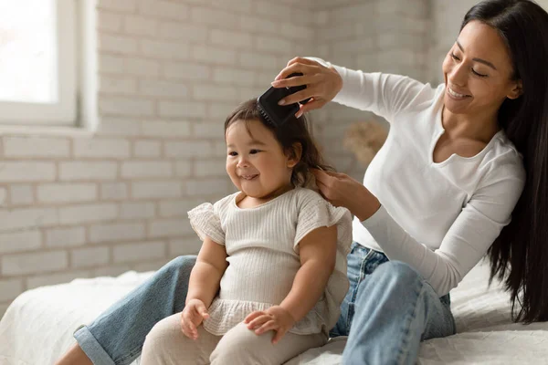 Happy Asian Mother Brushing Baby Daughters Hair Sitting Modern Bedroom — Stock Photo, Image
