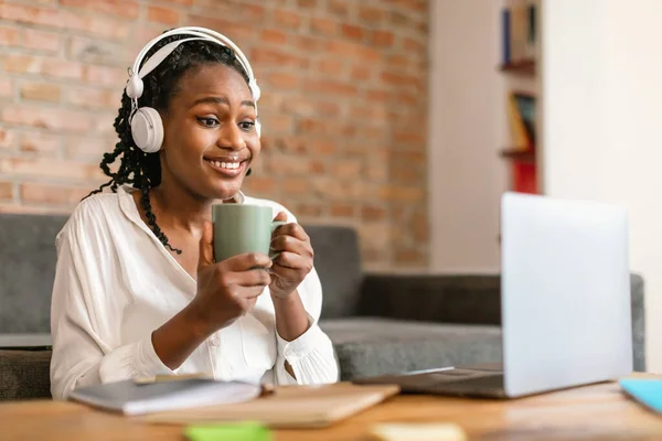 アフリカ系アメリカ人の女性は ラップトップを使用してワイヤレスヘッドフォンを着用し 自宅でオンラインで作業して通信します フリーランスのキャリアとリモートコミュニケーション — ストック写真