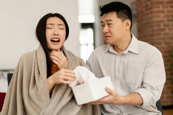 季节性过敏和鼻炎病 年轻的亚洲女人打喷嚏 关心自己的中年丈夫把纸巾送给妻子 坐在家里的沙发上 — 图库照片