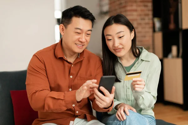 家庭网上购物 韩国丈夫和妻子使用手机和信用卡 通过智能手机在商店付款 坐在家里的沙发上 移动银行应用程序 — 图库照片