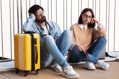 Üzüntülü, gündelik giyinmiş, gözlüklü, pasaportlu, biletli ve valizli genç çift havaalanında, şehirde, açık havada umutsuzluğa kapıldılar. Seyahat, tatil, seyahat sorunları ve hata için geç