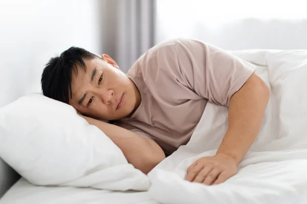 朝に一人でベッドに横たわっているパジャマを身に着けている不幸な不満を抱く中年のアジア人男性は 離婚や崩壊後のうつ病に苦しむ 立ち上がる意志がありません — ストック写真