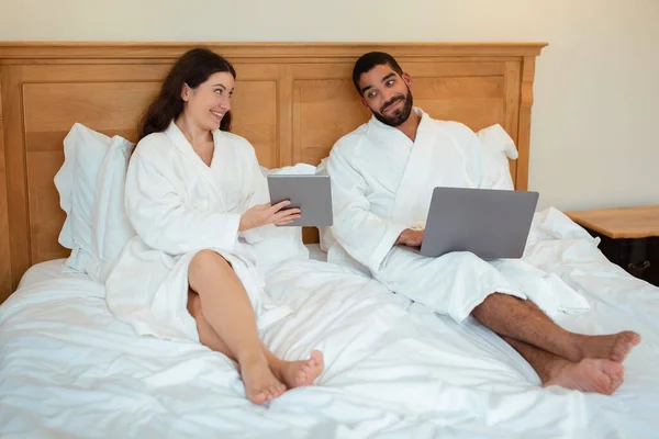 Neşeli Evdeki Modern Yatak Odasında Dizüstü Bilgisayarında Yatağında Otururken Kocasına — Stok fotoğraf