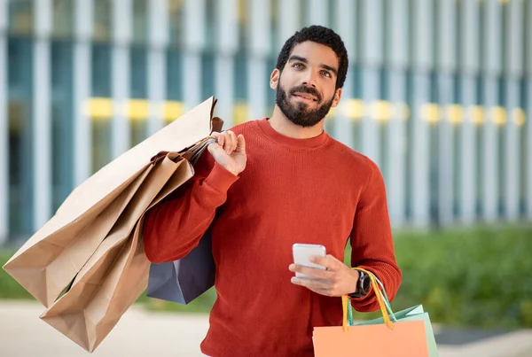 Uśmiechnięty Arabski Mężczyzna Zakupy Online Pomocą Telefonu Komórkowego Pozowanie Papierowych — Zdjęcie stockowe