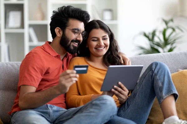 stock image Online Shopping Concept. Happy Indian Couple Using Digital Tablet And Credit Card At Home, Smiling Young Eastern Spouses Purchasing Things In Internet While Relaxing With Modern Gadget In Living Room