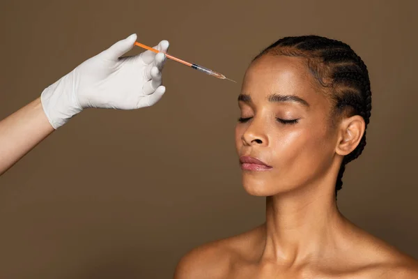 皮肤提升的概念 中年妇女在褐色背景下接受美容美发注射的头部照片 手拿着注射器戴防护手套的医生 — 图库照片