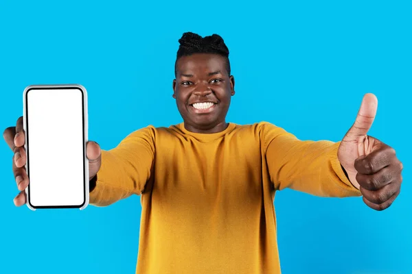 网上广告 快乐的年轻黑人男性用白色屏幕展示空白智能手机 并在相机前展示大拇指 微笑的非裔美国人推荐新的移动应用程序或网站Mockup — 图库照片