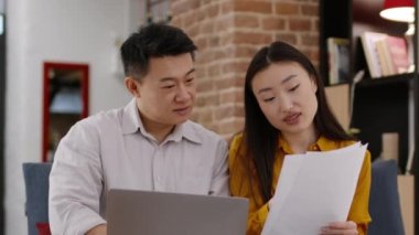 Evli Asyalı erkek ve kadının yakın plan portresi birlikte dizüstü bilgisayarda vergi formunu dolduruyor, kağıt paraları karşılaştırıyor, takip çekimleri, yavaş çekim, serbest alan