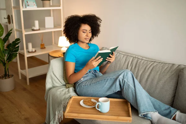 Alegre Libro Lectura Femenina Afroamericana Milenaria Disfrute Comida Beber Sofá —  Fotos de Stock