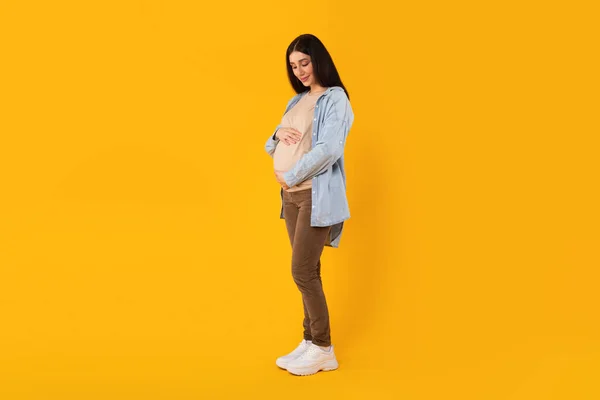 全身上下拍摄的孕妇手挽着大肚子隔离在黄色的工作室背景 自由自在的空间 期望概念 — 图库照片