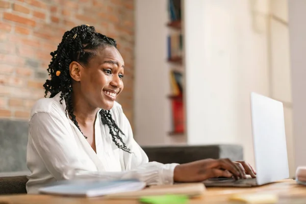 ラップトップで入力するアフリカ系アメリカ人女性の笑顔 自宅からオンラインで働くか 自由空間 ビジネスはリモートで ウェブサイトでのフリーランスと自宅で新しい通常 — ストック写真