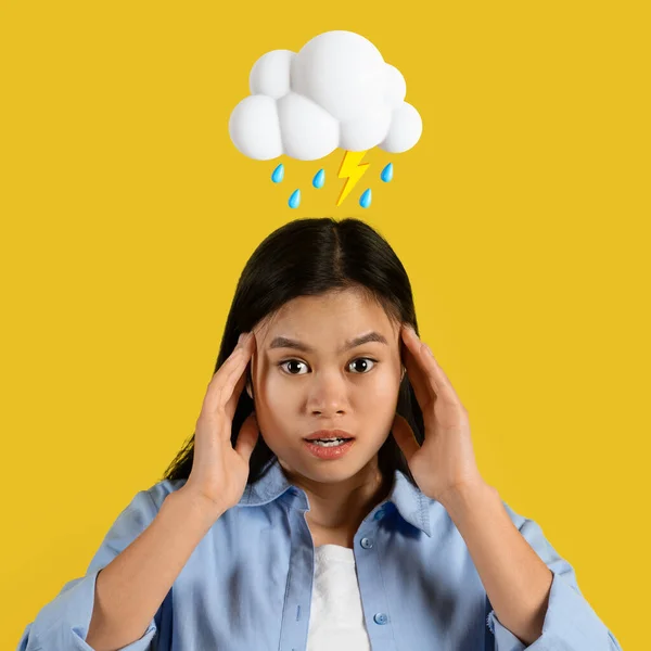 Shocked sad young asian woman hold head with hands with abstract cloud of lightning and rain sign above head isolated on yellow studio background. Migraine, stress, negative human emotion