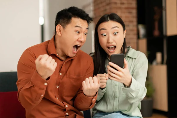 Emotioneel Aziatisch Koppel Viert Succes Kijkt Naar Mobiele Telefoon Scherm — Stockfoto