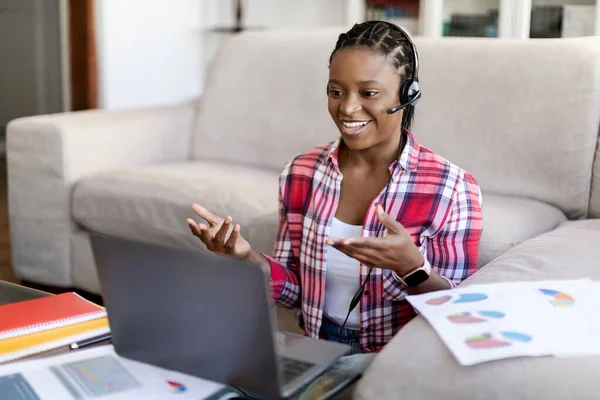 カジュアルな服装の従業員 自宅から働く独立した請負業者で幸せな肯定的な笑顔若い黒人女性は コンピュータやヘッドセットを使用して チームやクライアントとオンライン会議を持っています — ストック写真