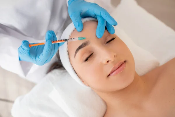 Aesthetic Treatment. Young beautiful woman getting injection on forehead in salon, closeup shot of unrecognizable beautician doctor making beauty shot to female patient in modern clinic