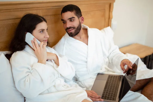 Férj Megmutatja Laptop Számítógép Feleségének Miközben Beszél Telefonon Ágyban Beltéri — Stock Fotó